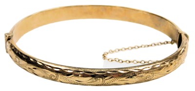 Lot 555 - A 9ct gold bangle, with engraved foliate...