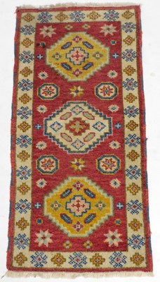 Lot 754 - A Kazak red ground rug, decorated with three...